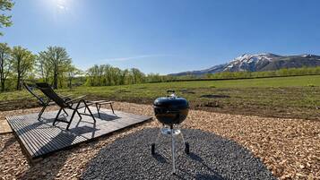 A barbecue grill on a wooden deck with a view of a mountain range.
