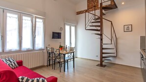 A modern living room with a red sofa, a dining table with chairs, a spiral staircase, and a TV mounted on the wall. - Cozy and bright apartment, located a few meters from the tramway! (Firenze)