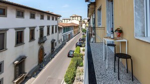 A narrow street with buildings on either side, a balcony with a table and chairs, and a clear sky. - Cozy and bright apartment, located a few meters from the tramway! (Firenze)