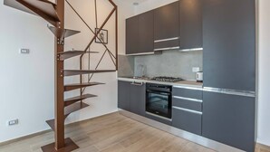 A modern kitchen with dark cabinetry, a gas stove, and a built-in oven. A spiral staircase with a metal frame is visible to the left. - Cozy and bright apartment, located a few meters from the tramway! (Firenze)