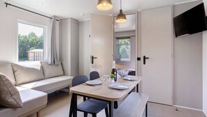 Een moderne kamer met een bank, een eettafel, stoelen, een televisie en een raam met uitzicht.