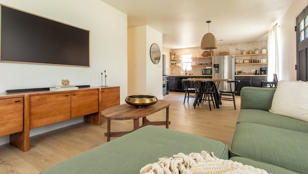 Ein modernes Wohnzimmer mit einem grünen Sofa, einem Holztisch und einer großen Tafel an der Wand.