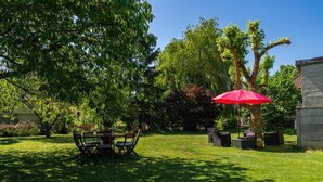 Eine Terrasse mit Tisch und Stühlen, umgeben von Bäumen und einem roten Sonnenschirm.