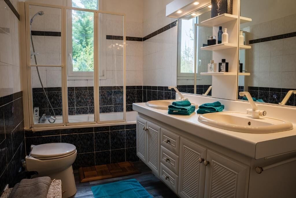 A bathroom with two sinks, a toilet, a shower, and a window with a view of trees.