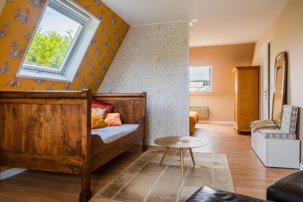 A bedroom with a sloped ceiling, a wooden bed, a round coffee table, and a view of the outdoors.