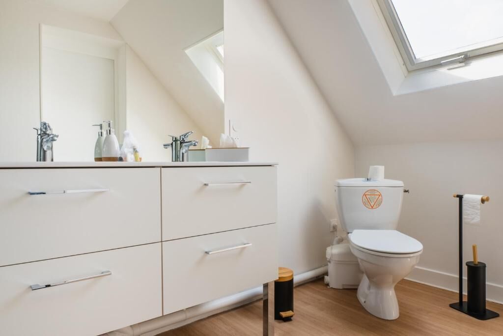 A modern bathroom with a skylight, white vanity with drawers, a toilet, and a bidet.