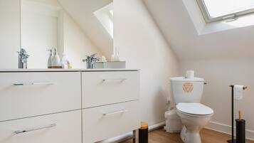A modern bathroom with a skylight, white vanity with drawers, a toilet, and a bidet.