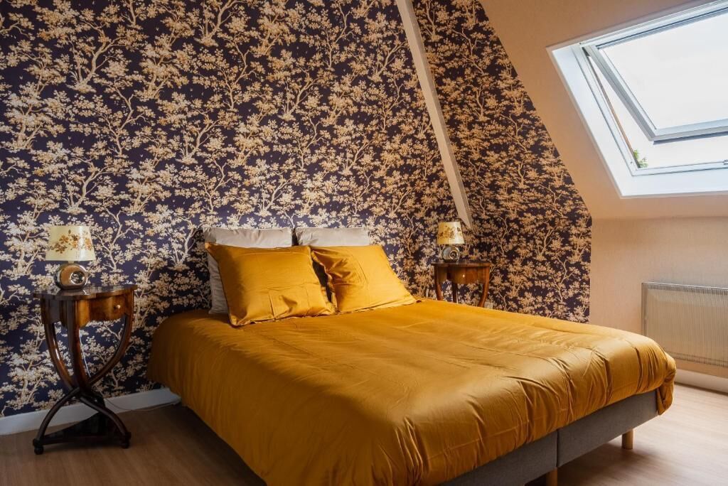 A bedroom with a bed, floral wallpaper, and a skylight.