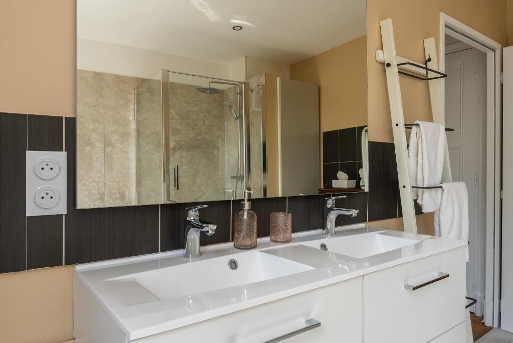 A modern bathroom with two sinks, a large mirror, and a towel rack.