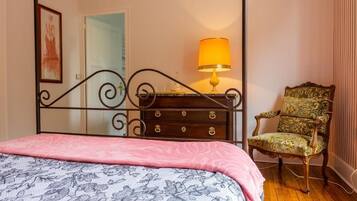Een slaapkamer met een hemelbed, een dressoir met een lamp en een bloemen fauteuil.