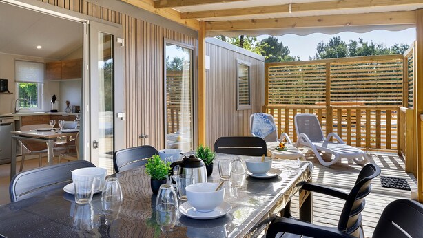 A covered outdoor dining area with a table set for two, chairs, and a view of the backyard. - “Evasion 55” Mobile Home with Shared Pool and Terrace (Saint-Gervais)
