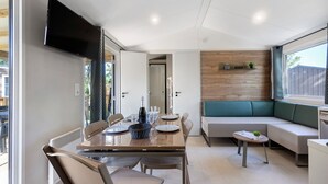 A modern kitchen with a dining area, a built-in bench, and a television mounted on the wall. - “Evasion 55” Mobile Home with Shared Pool and Terrace (Saint-Gervais)