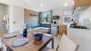 A compact kitchen with a built-in stove, a dining area with a table set for two, and a seating area with a bench. - “Evasion 55” Mobile Home with Shared Pool and Terrace (Saint-Gervais)