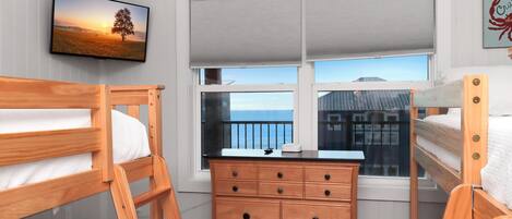 Ett sovrum med två våningssängar, en byrå i trä, en tv och ett fönster med utsikt över havet.