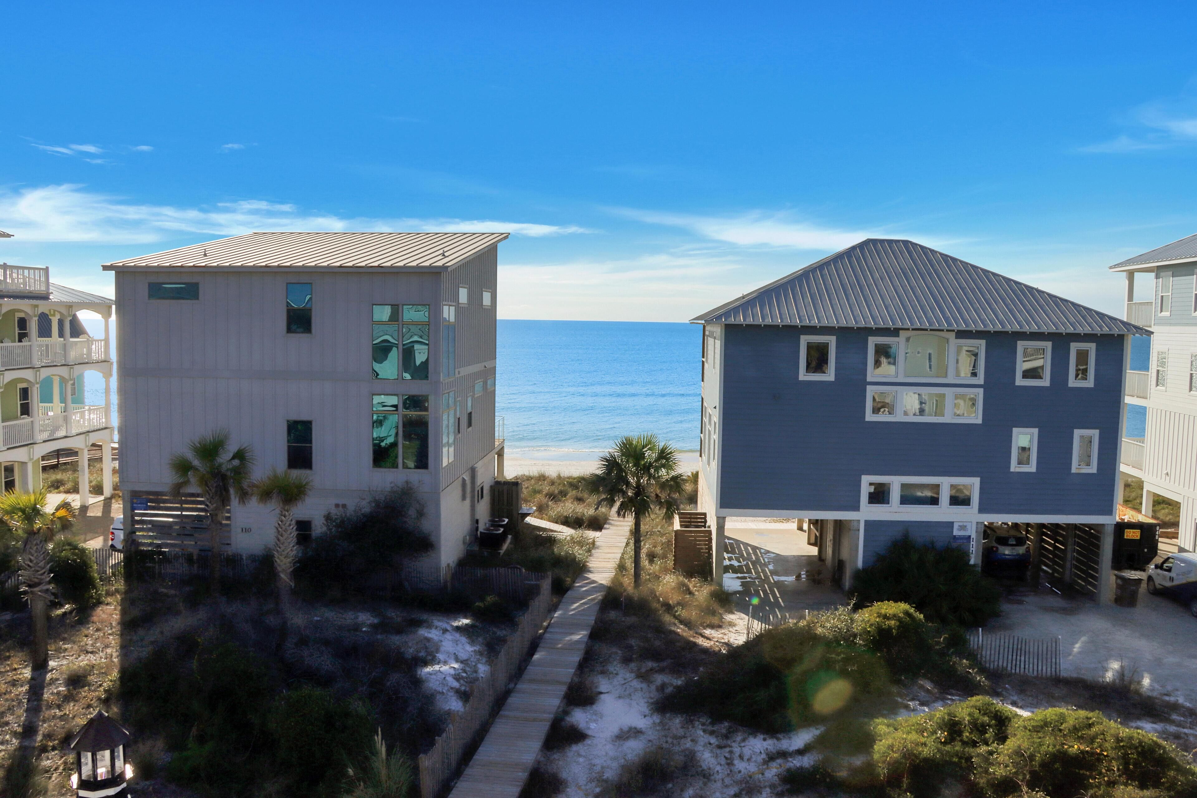 A coastal building with a view of the ocean, a wooden pathway, and a parking area.