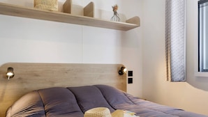 Ein Schlafzimmer mit einem hölzernen Kopfteil, einem Bett mit dunkler Bettdecke, einem gewebten Hut und einem gepunkteten Kissen.