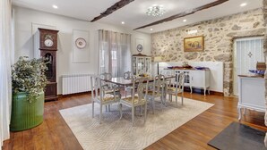 Un comedor con una mesa y sillas de madera, una planta verde, un reloj y una pared de piedra.