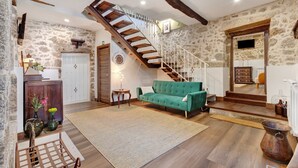 Amplia sala de estar con escalera, sofá verde y pared de piedra rústica.