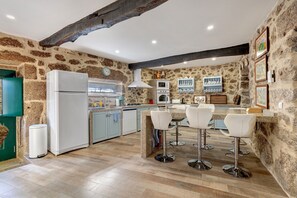 A kitchen with stone walls, a wooden ceiling, and a bar area with stools. - Holiday Home 'Casa Do Forno' with Mountain View, Wi-Fi & Air Conditioning (Ponte da Barca)