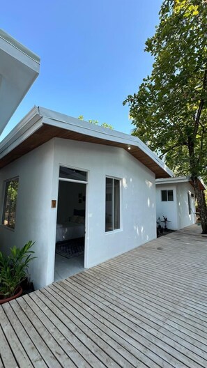 Ett modernt hus med en träveranda, en stor, öppen dörröppning och ett litet fönster.