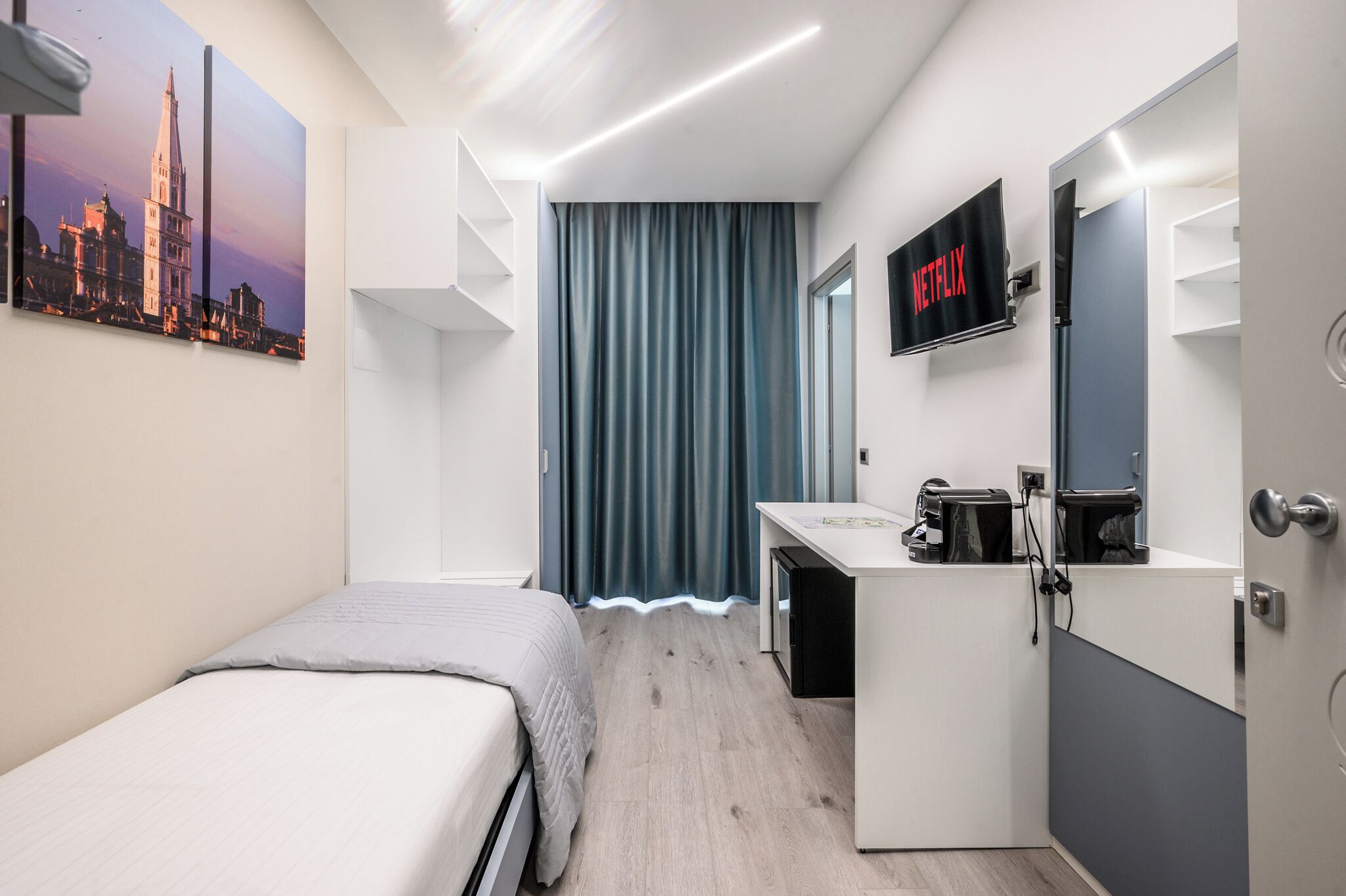 A modern hotel room with a bed, a desk, a flat-screen TV, and a large window with curtains.