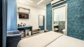 Une chambre d’hôtel moderne équipée d’un lit, d’un bureau avec un ordinateur, d’une télévision affichant « NETFLIX », et d’une salle de bain avec un miroir et des toilettes.