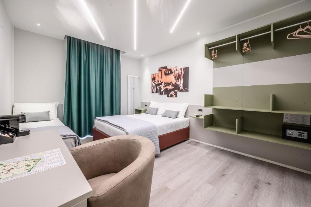 A modern hotel room with a bed, a desk, a chair, a wardrobe, and a wall-mounted TV.