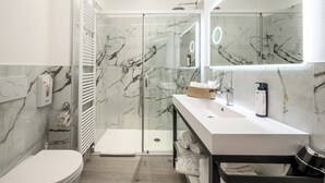 Une salle de bain moderne avec une douche à parois de verre, un lavabo blanc et un mur recouvert de carreaux de marbre.