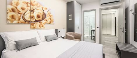 A modern hotel room with a large bed, a desk, a chair, and a wall-mounted air conditioner.