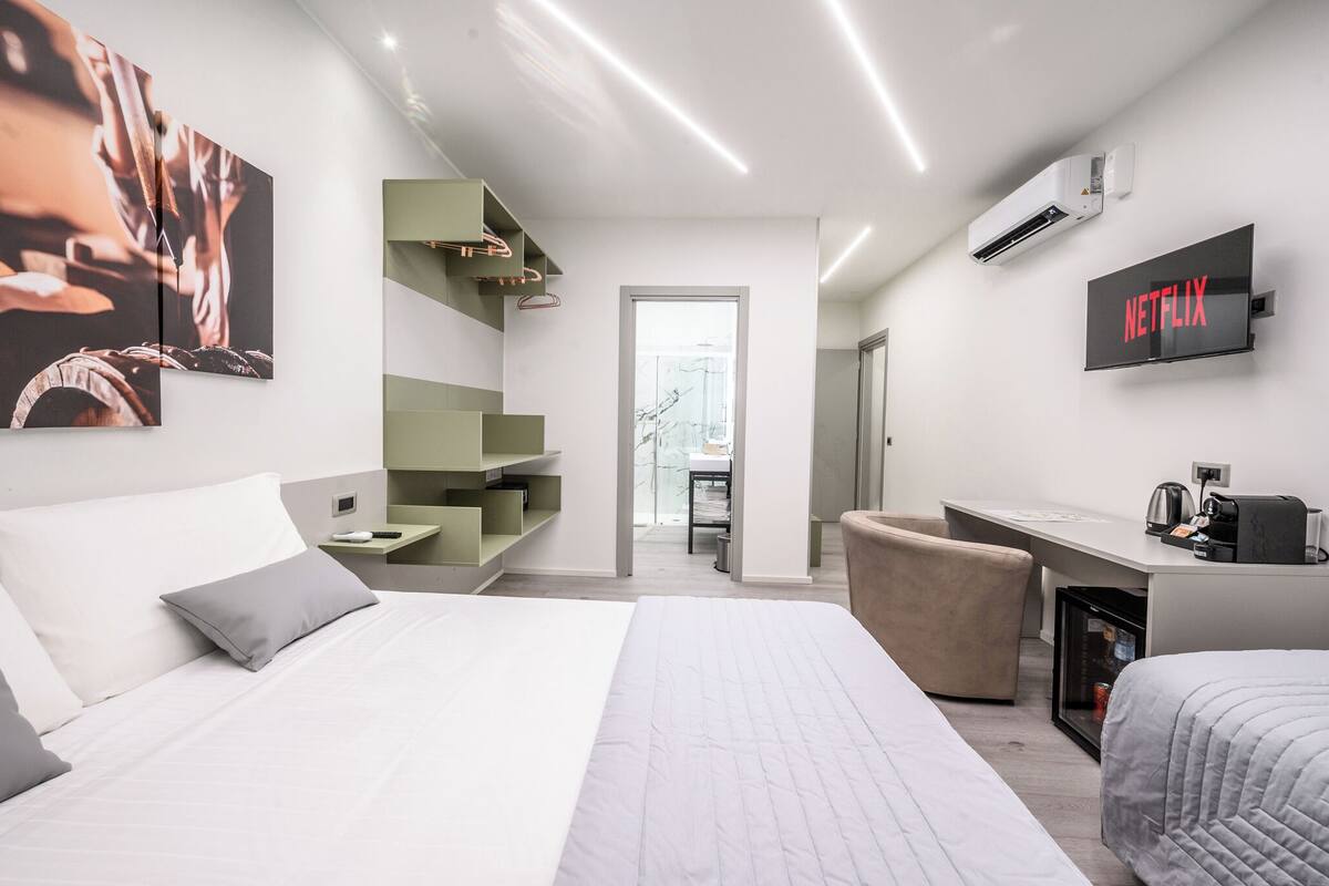 A modern hotel room with a large bed, a desk with a computer, a TV, and a wardrobe.