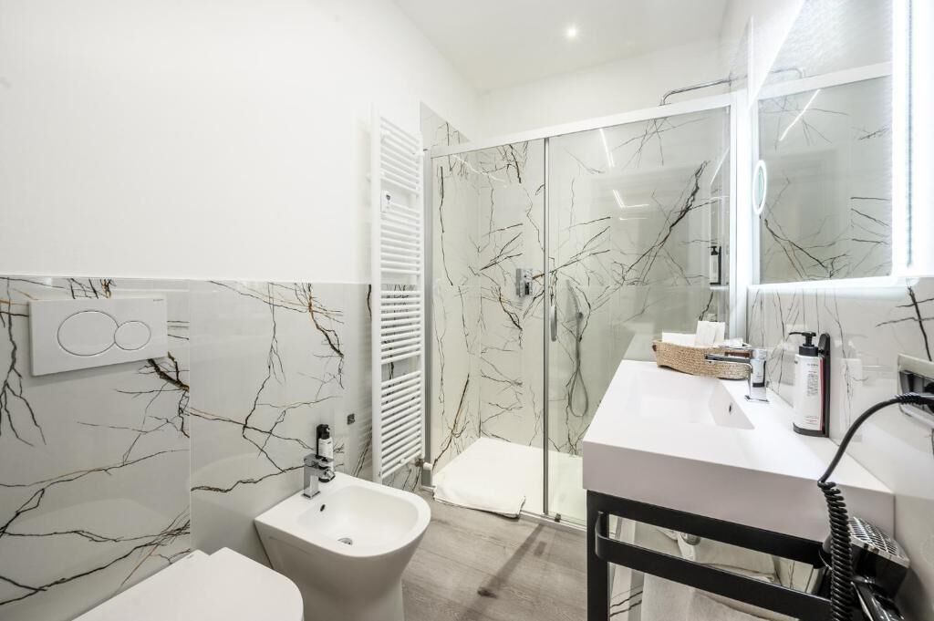 A modern bathroom with a marble backsplash, a bidet, a shower enclosure, and a vanity with toiletries.