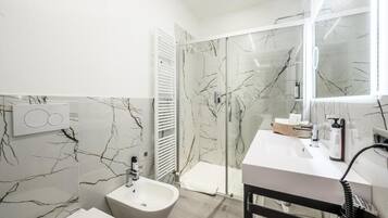Un bagno moderno con rivestimento in marmo, un bidet, cabina doccia e mobile lavabo con articoli da toilette.