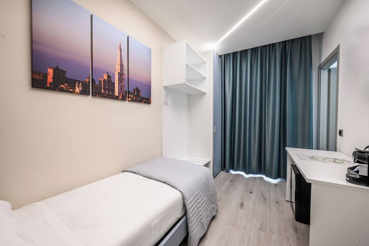 A hotel room with a bed, a desk, and a large window with curtains.