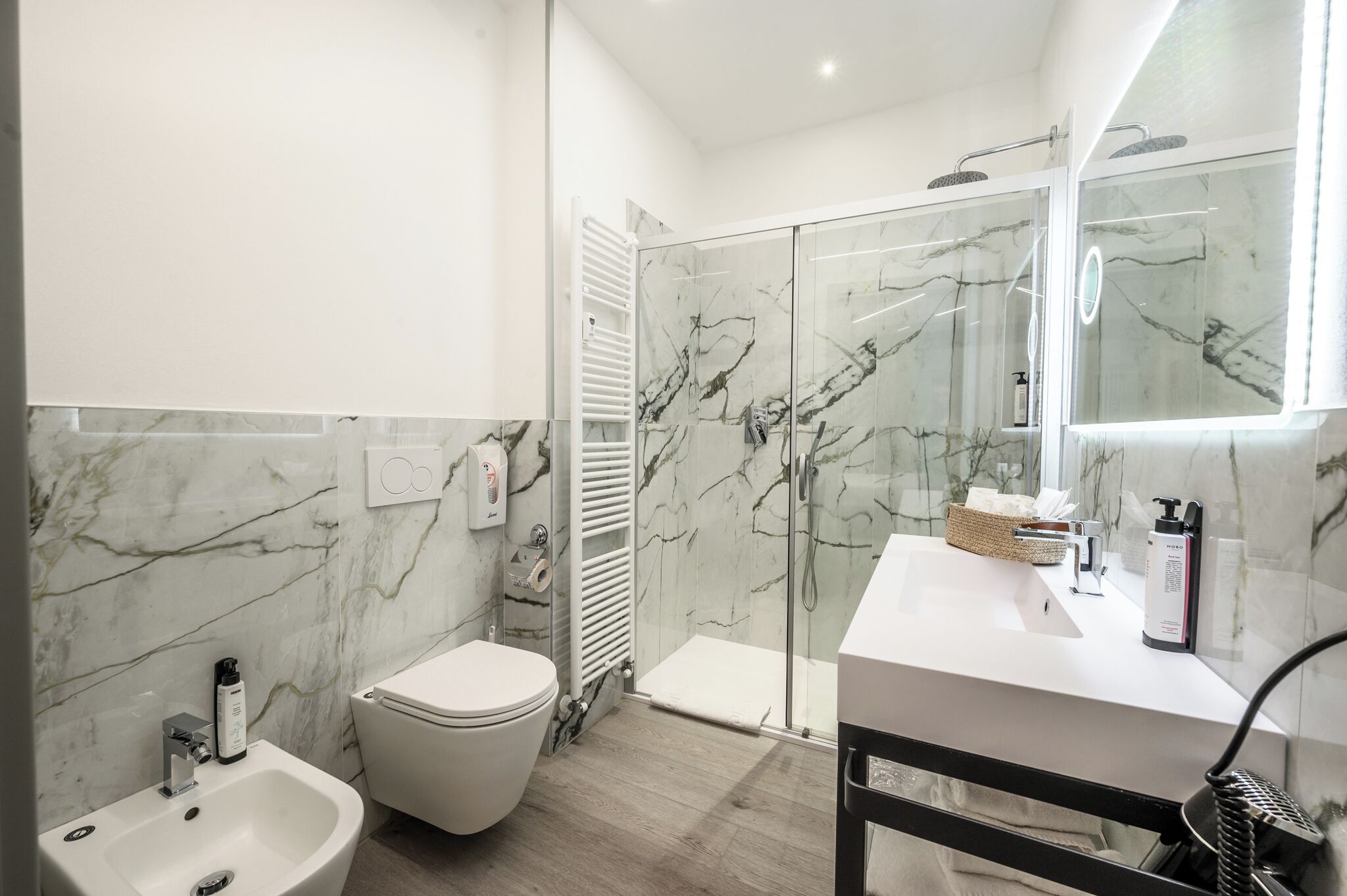 Ein modernes Badezimmer mit Marmorverkleidung, einem weißen Waschbecken, einer Toilette und einer Duschkabine.
