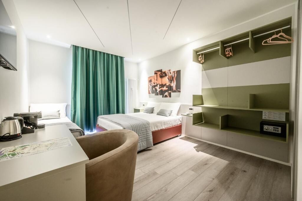 Een moderne hotelkamer met een bed, een bureau, een stoel, een kledingkast en een schilderij aan de muur.