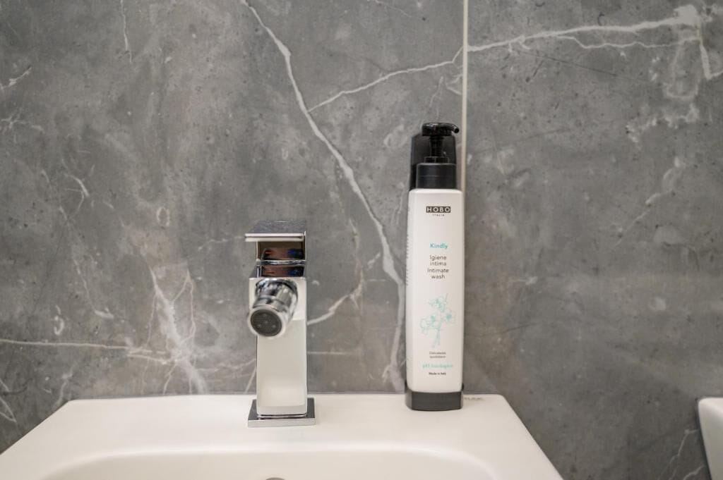 A bathroom with a modern sink, a chrome faucet, and a bottle of hygiene product.