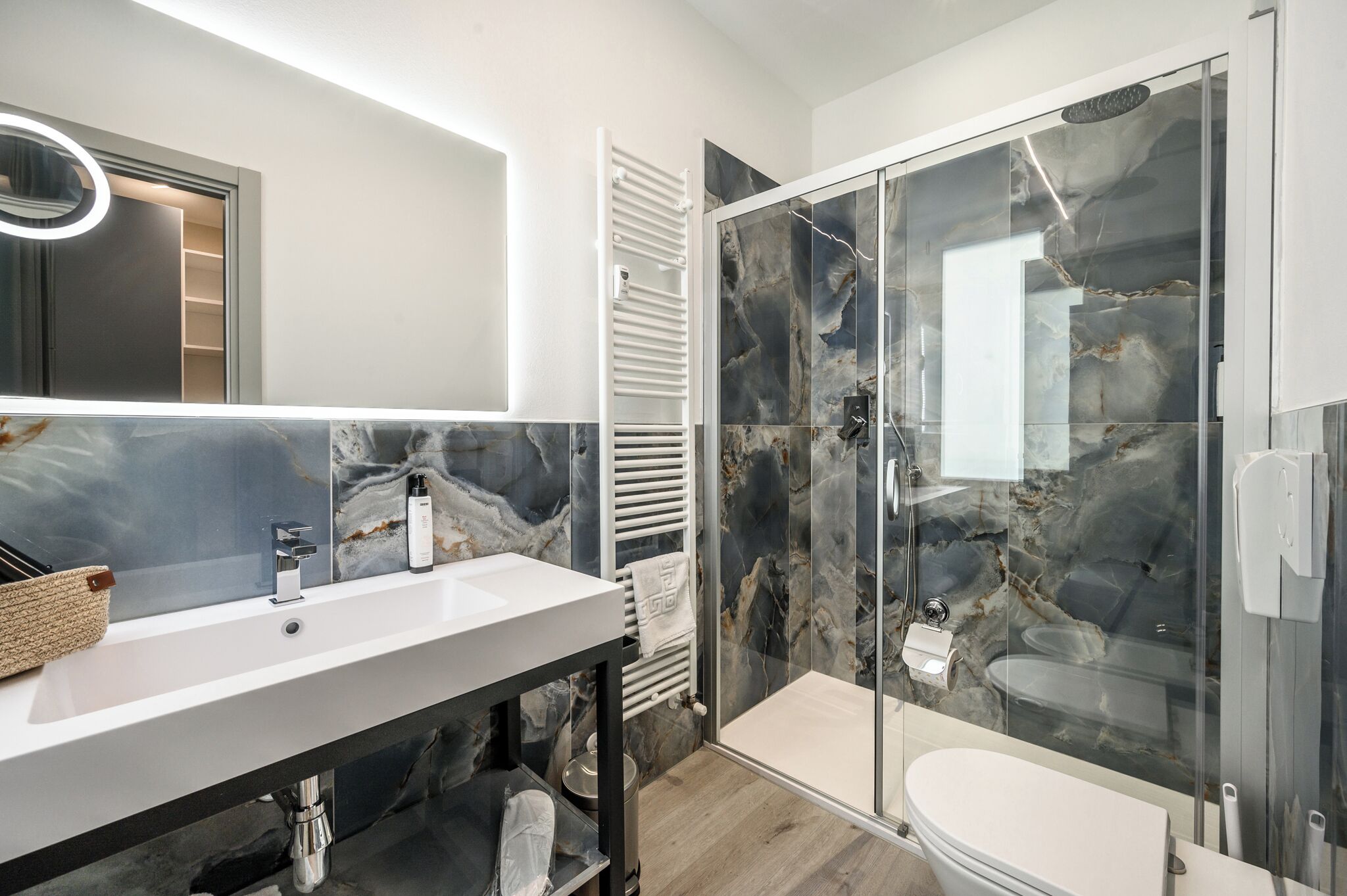A modern bathroom with a white sink, a glass shower enclosure, and marble walls.