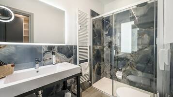 A modern bathroom with a white sink, a glass shower enclosure, and marble walls.