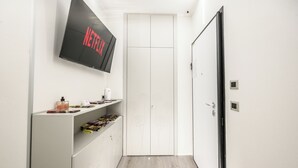 Un couloir étroit avec une armoire blanche, un téléviseur fixé au mur qui affiche le logo « NETFLIX », et une étagère contenant divers objets.