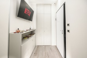 Kapea käytävä, jossa on valkoinen vaatekaappi, seinälle asennettu televisio, jossa näkyy teksti »NETFLIX», ja hylly, jossa on erilaisia esineitä.