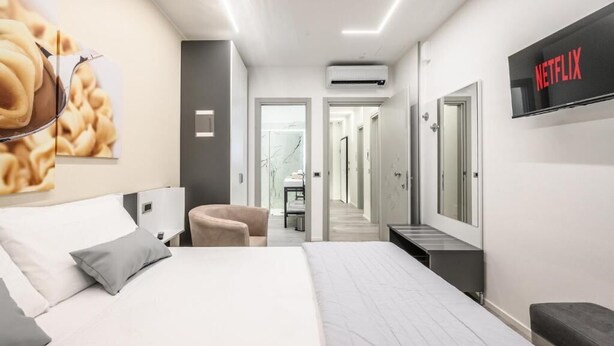 Une chambre d’hôtel moderne, dotée d’un grand lit, d’un téléviseur fixé au mur et d’un couloir menant à d’autres chambres.