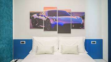 A hotel room with a large bed, white bedding, a blue headboard, and a wall-mounted artwork of a blue sports car.