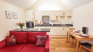 A compact living space with a kitchenette, a red sofa with floral cushions, a dining table with chairs, and a small TV. - The Stables (Louth)