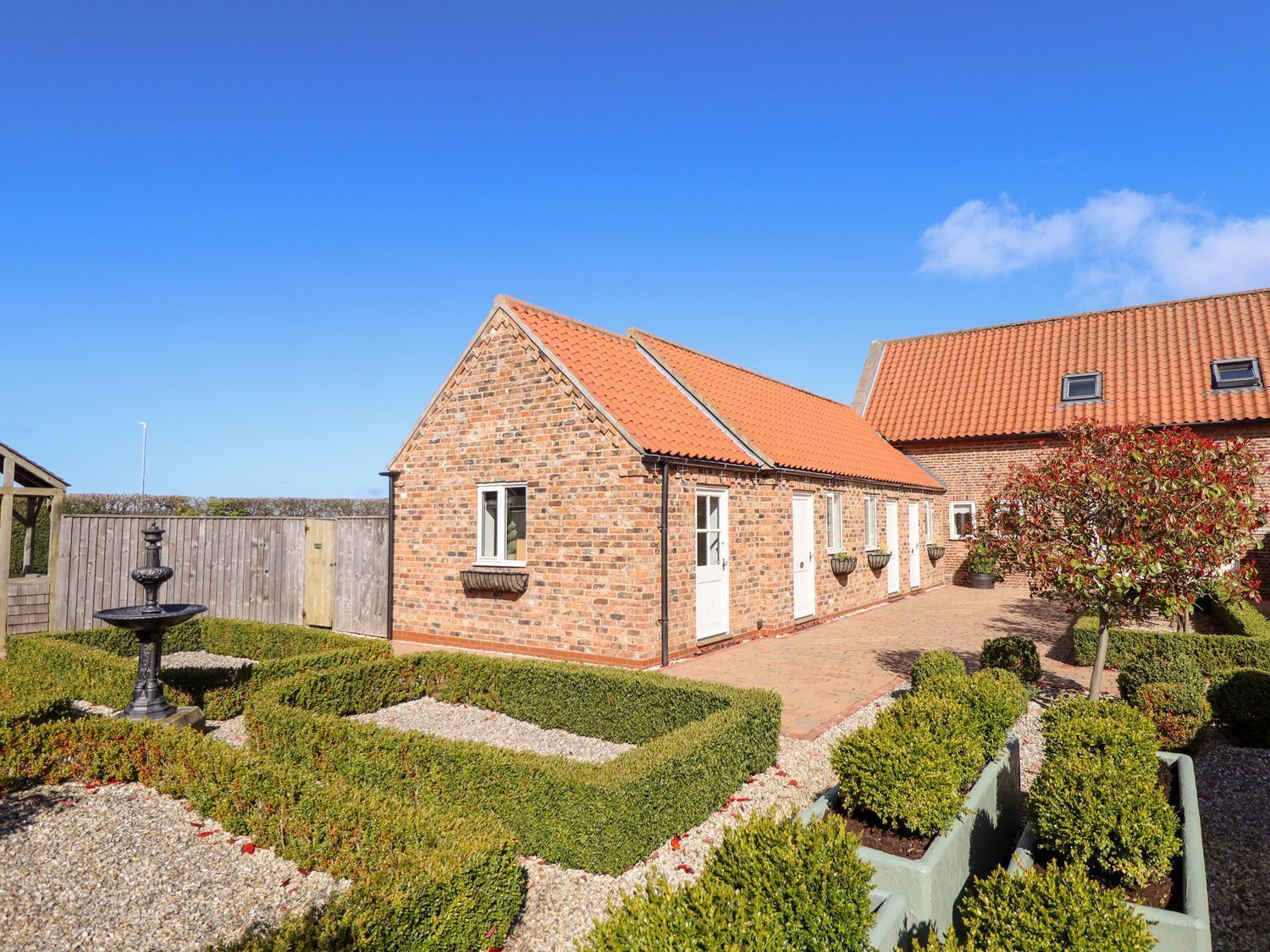 A brick building with a tiled roof, a fountain, and a well-maintained garden with hedges and gravel paths.