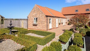 A brick building with a tiled roof, a fountain, and a well-maintained garden with hedges and gravel paths. - The Stables (Louth)