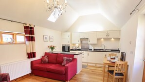 A compact living space with a red sofa, a dining table with chairs, a kitchen area, and a chandelier. - The Stables (Louth)