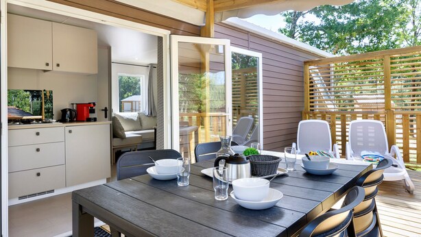 Eine Holzdar Terrasse mit Esstisch für zwei Personen, einer Küchenzeile mit Schränken und Blick ins Freie.