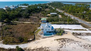 An aerial view of a coastal property with a large house featuring a swimming pool, surrounded by dense vegetation and a beach. - Indian Shores Cottage (Port St. Joe)