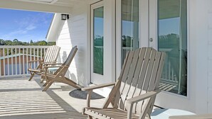 A covered deck with wooden chairs and a glass door leading to a pool area. - Indian Shores Cottage (Port St. Joe)