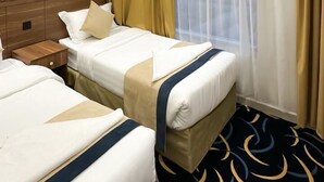 A hotel room with two beds, a wooden headboard, a nightstand, and a large window with sheer curtains.